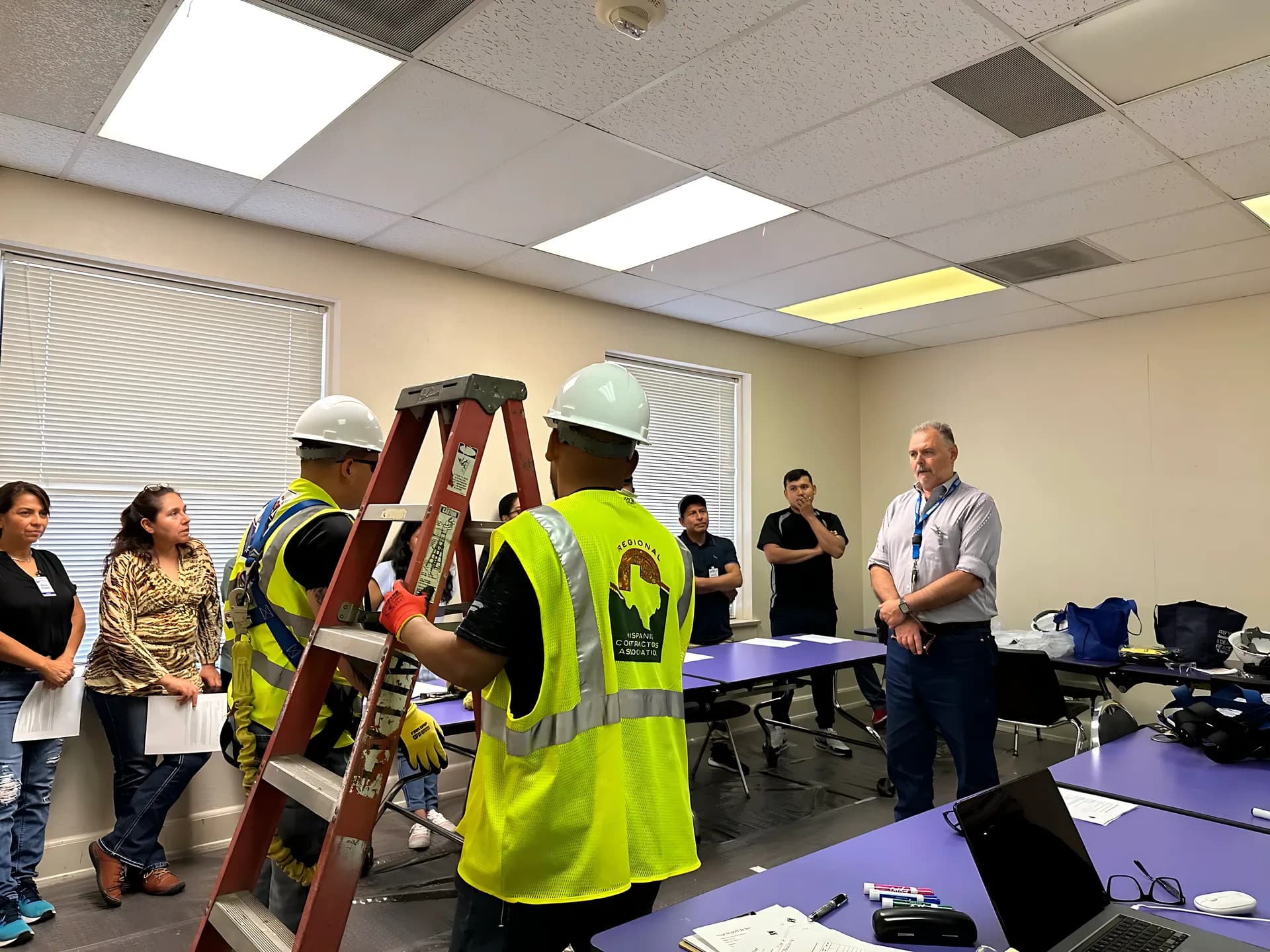Participants wearing hard hats and safety vests practice with a ladder during a construction training session.