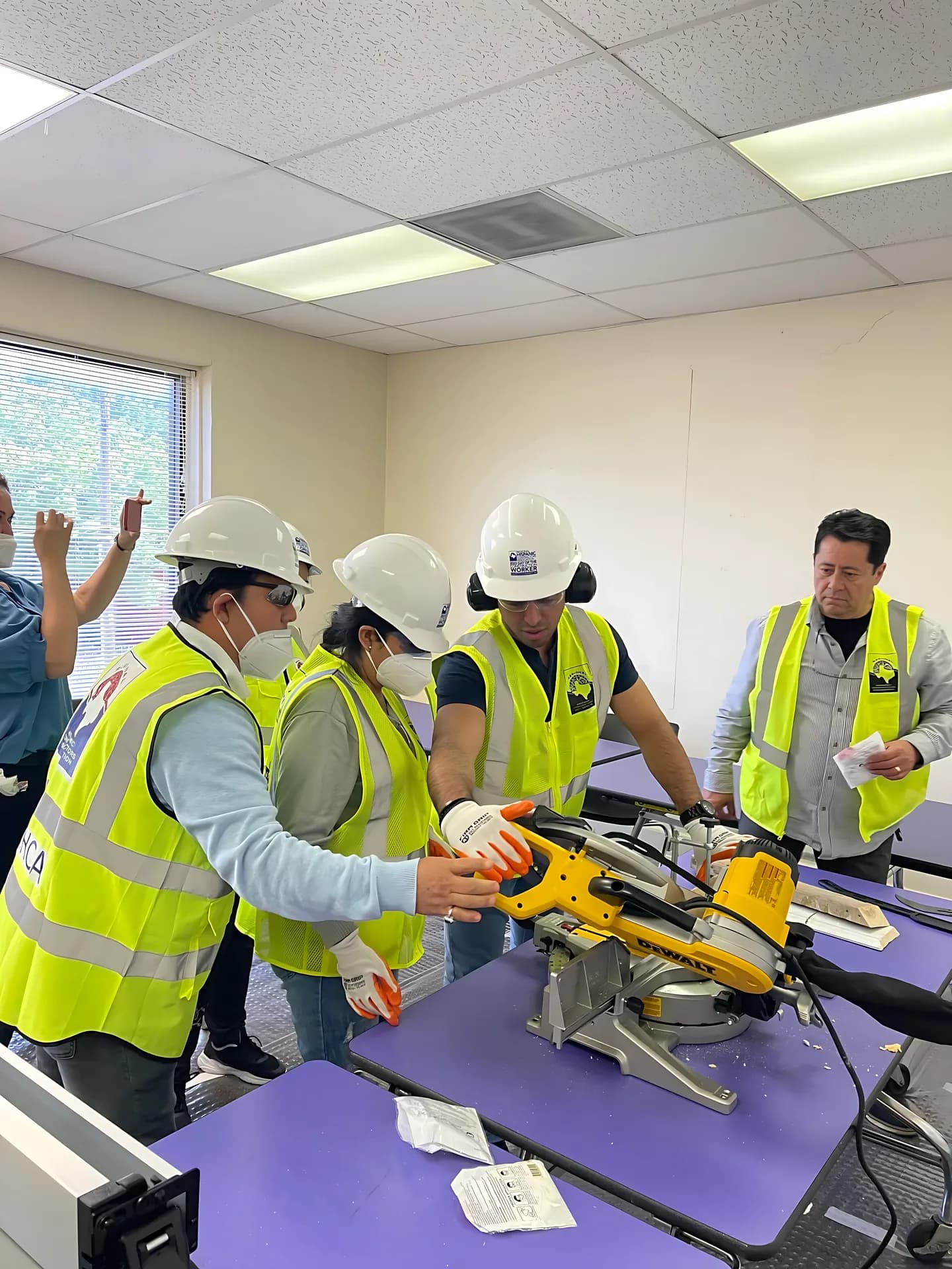 Construction trainees gathered around a miter saw during a classroom exercise.