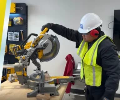 Trainee in a hard hat and safety vest operating a miter saw at the RHCA training center