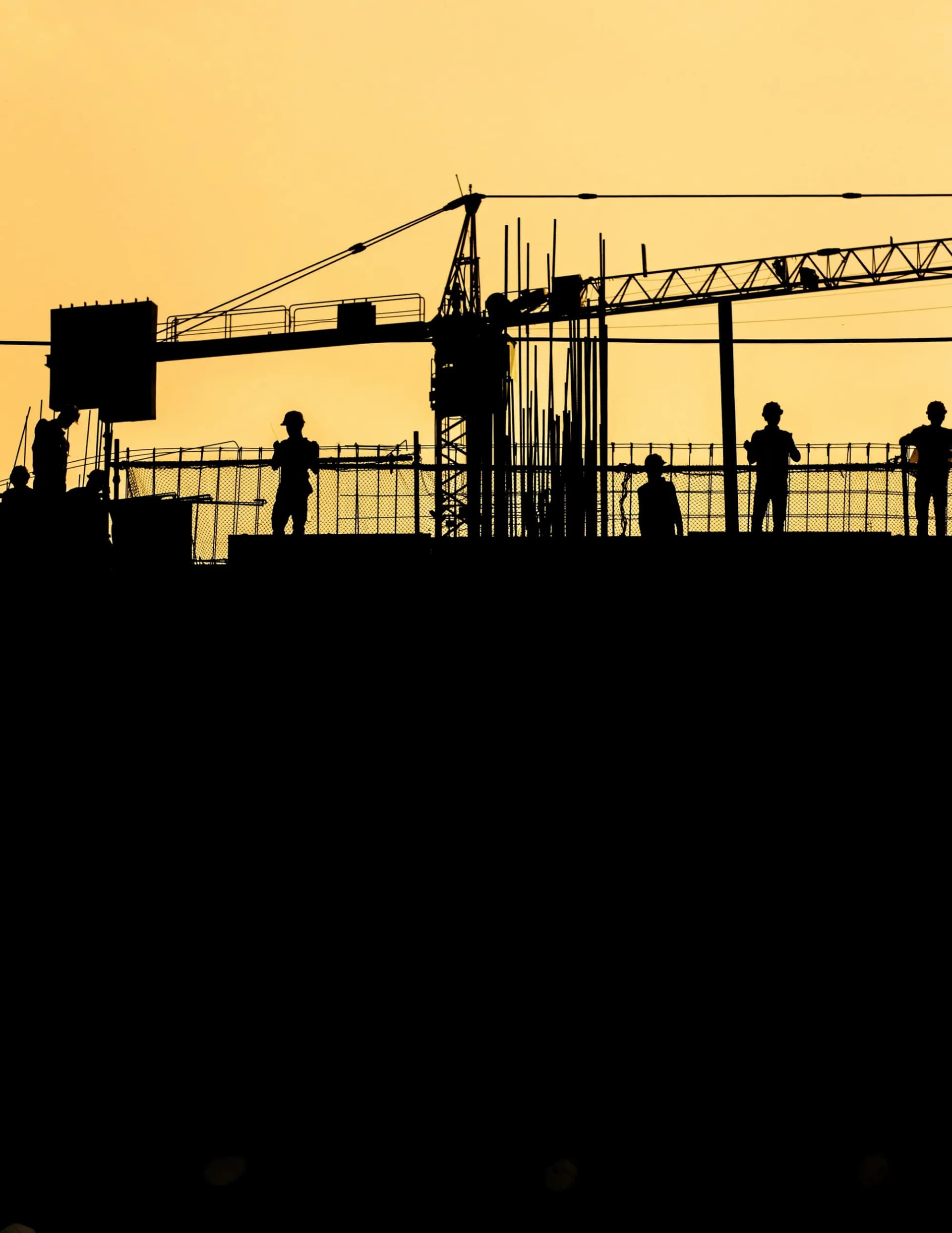 Construction workers silhouetted at sunset.