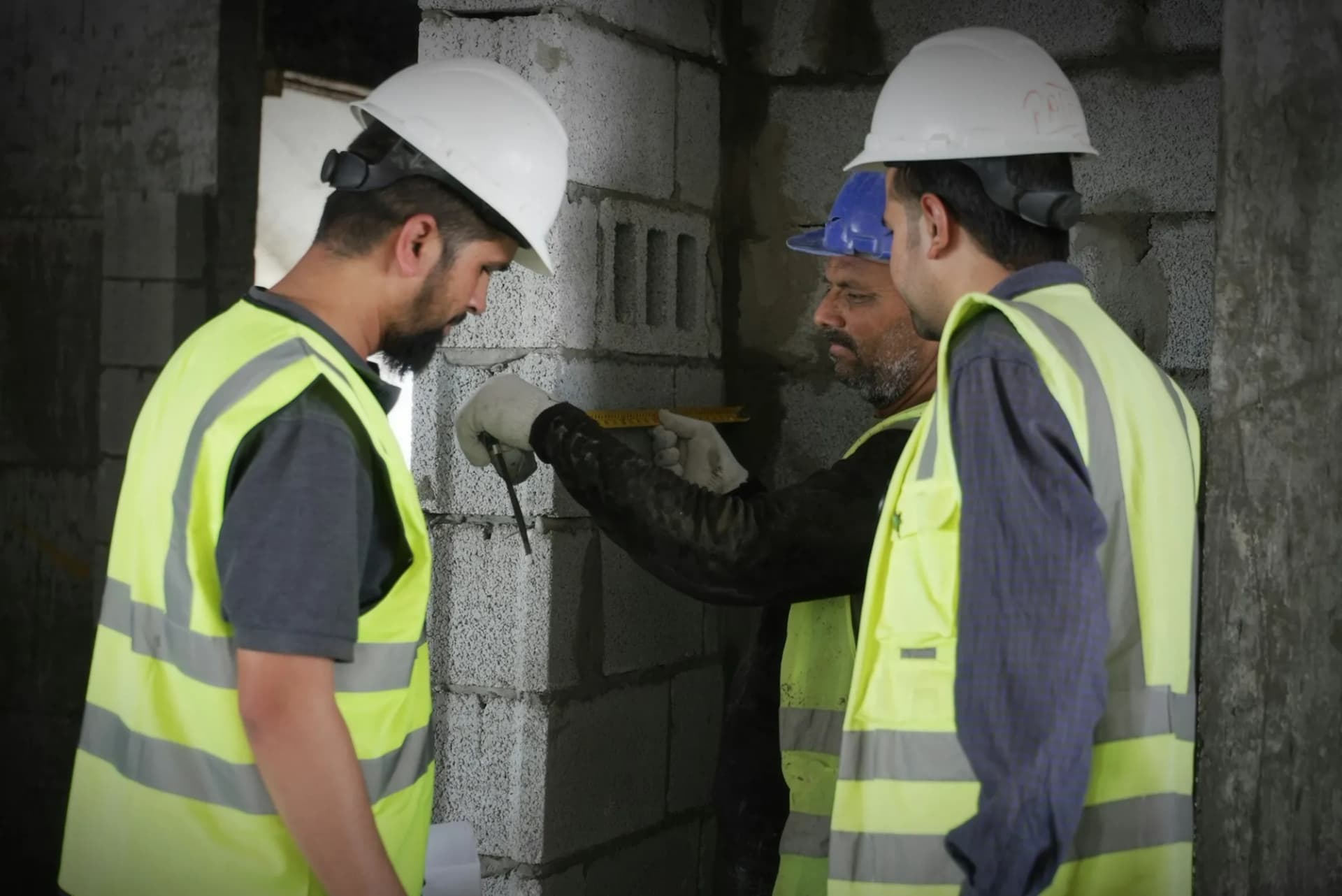 Three construction workers in safety gear measuring a concrete wall